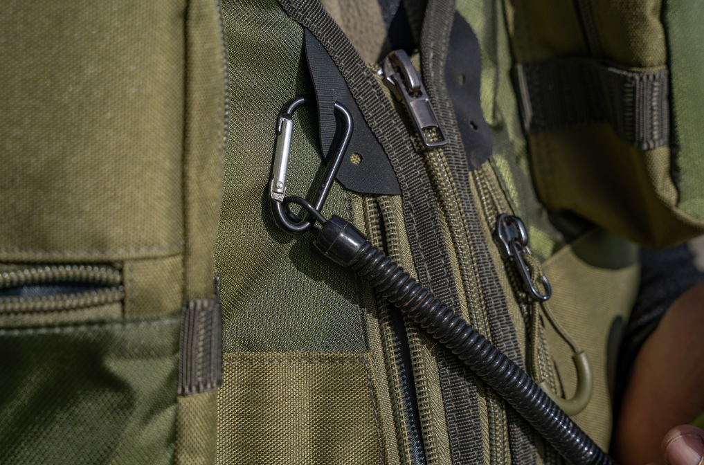 Мултифункционални клещи с карабинер KORUM Multi Tool With QC Lanyard, показан с разтегателен кабел на зелен джоб.
