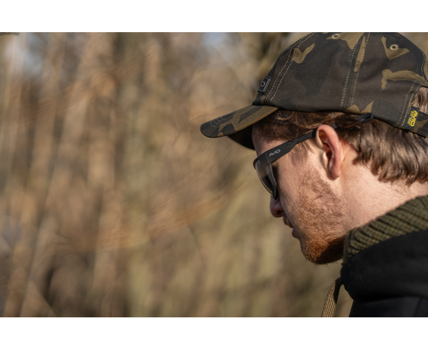 Поляризирани слънчеви очила AVID CARP SeeThru OptiWrap Grey Lens на мъж с камуфлажна шапка на открито.