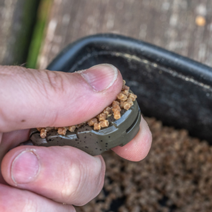 Олово KORUM Bait Gripper Leads being filled with bait during fishing preparation.