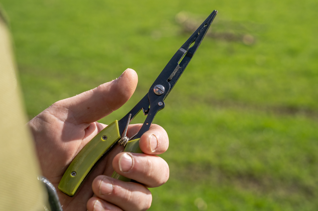 Мултифункционални клещи с карабинер KORUM Multi Tool With QC Lanyard в ръка на зелен фон.