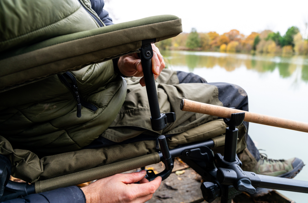 Човек настройва луксозен фидер стол KORUM S23² Supa Deluxe Accessory Chair близо до вода.