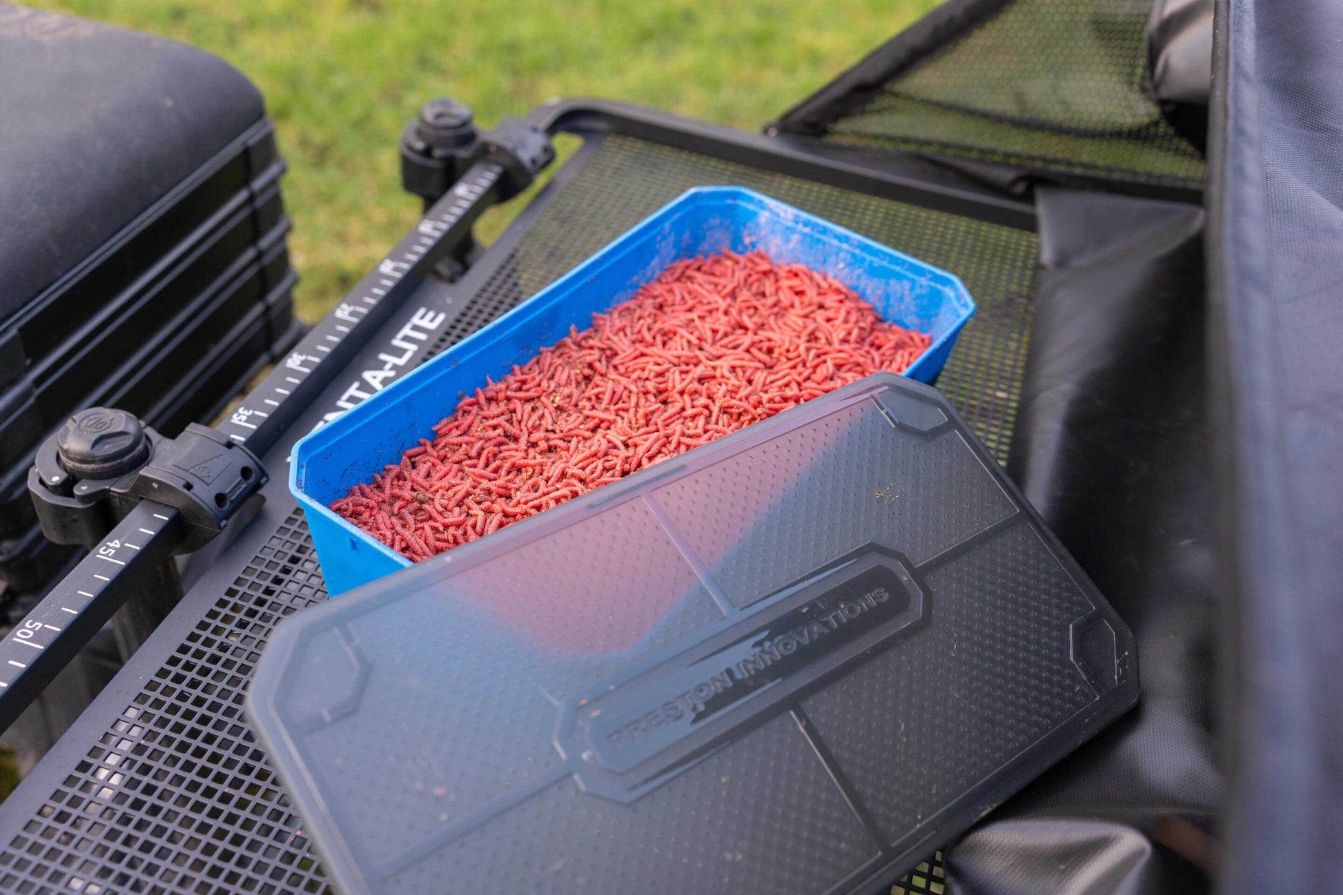 Кутия за стръв PRESTON 6PT BAIT TUB с червени стръв, поставена на риболовна маса.