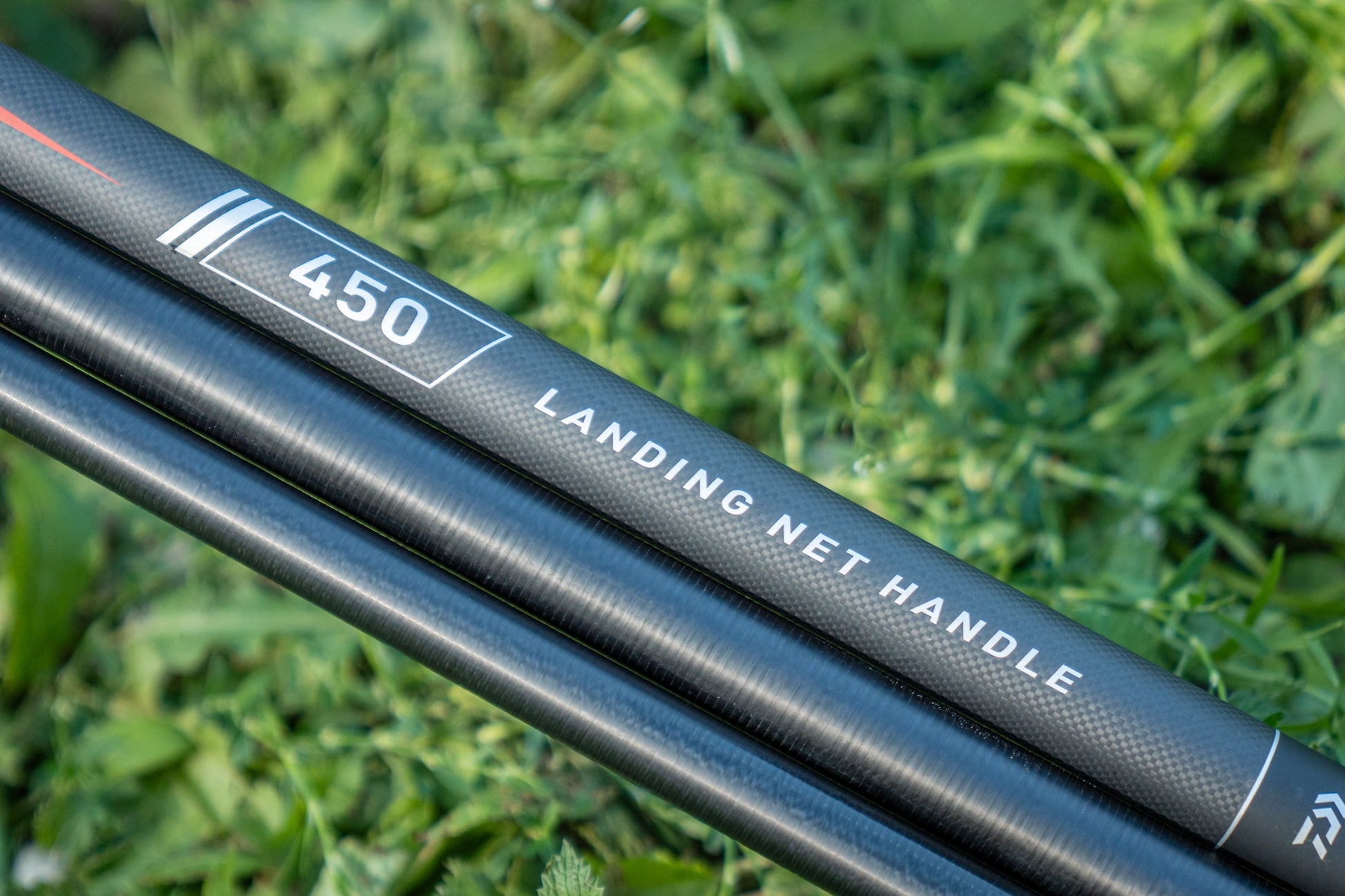 Дръжка за кеп DAIWA 25 AIR LANDING NET HANDLE 4.50m на фона на зелена трева.