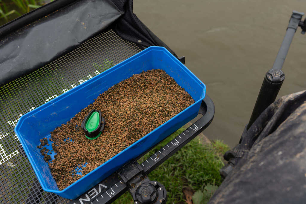 Кутия за стръв PRESTON 6PT BAIT TUB с примамка на риболовно място близо до вода.