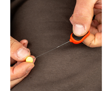 Игла - AVID RE-RIG FINE HAIR NEEDLE in use with a small yellow bait, demonstrating ergonomic grip.