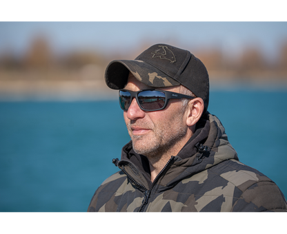 Мъж с поляризирани слънчеви очила AVID CARP SeeThru OptiWrap Grey Lens, стоящ на открито до вода.