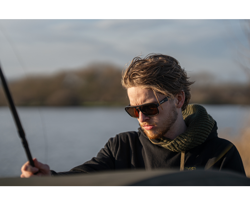 Мъж с поляризирани слънчеви очила AVID CARP SeeThru AV Classic Polarised Sunglasses, риболов на фона на езеро.