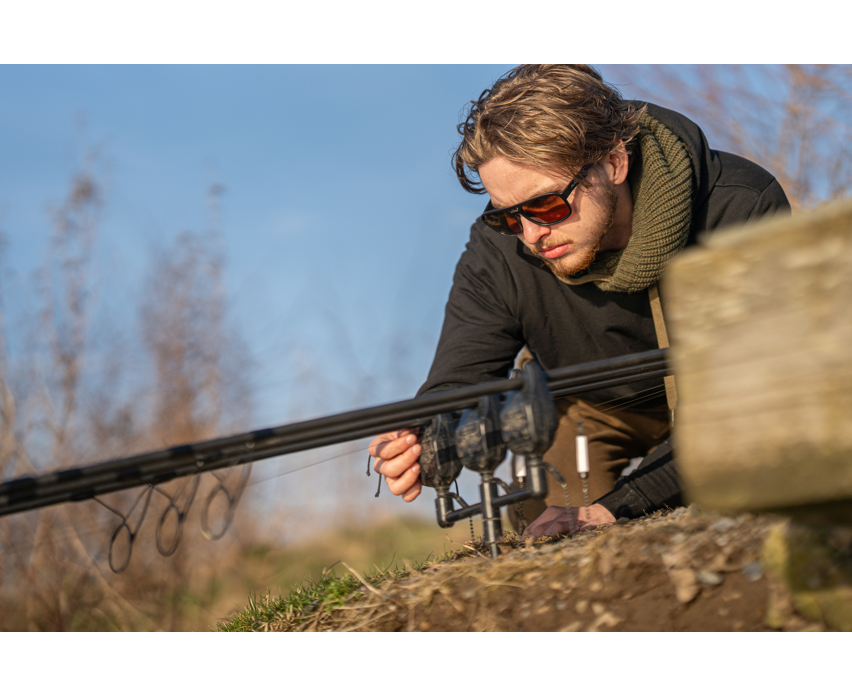 Мъж с поляризирани слънчеви очила AVID CARP SeeThru AV Classic Polarised Sunglasses, фокусира се върху риболова.