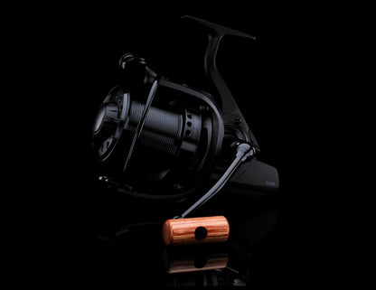 Шаранджийска макара Daiwa 17 BASIA 45 SLD QD с дървена ръкохватка на черен фон.