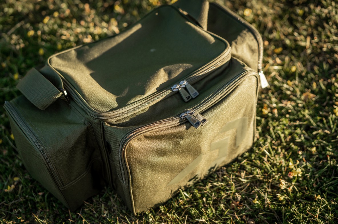 Сак DAIWA BLACK WIDOW COMPACT TACKLE BAG on grass, showcasing its quality design and zippers.