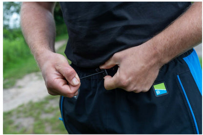Водоустойчив панталон PRESTON DF ULTRA TROUSERS, затягане на колана от риболовец на открито.