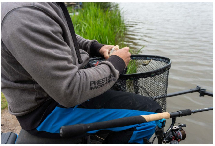 Водоустойчив панталон PRESTON DF ULTRA TROUSERS - риболовец задържащ риба в кабинката до водоем.