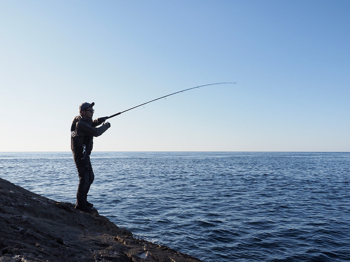 Риболовец с спининг въдици за shore jigging риболов DAIWA Dragger SX на скалиста брегова линия.