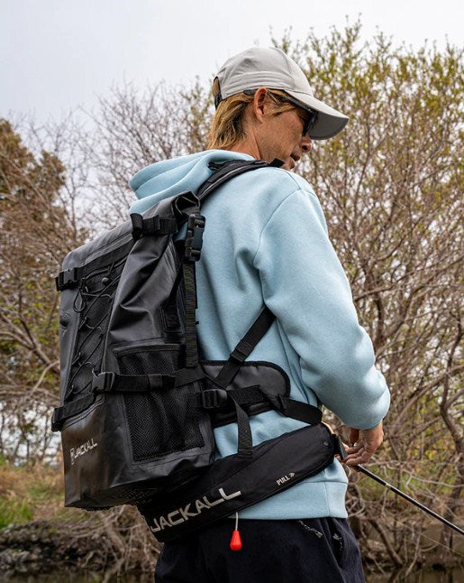 Водоустойчива чанта за спининг риболов JACKALL WATERPROOF BACKPACK L (30L - 35L) - Черна, носена от риболовец.