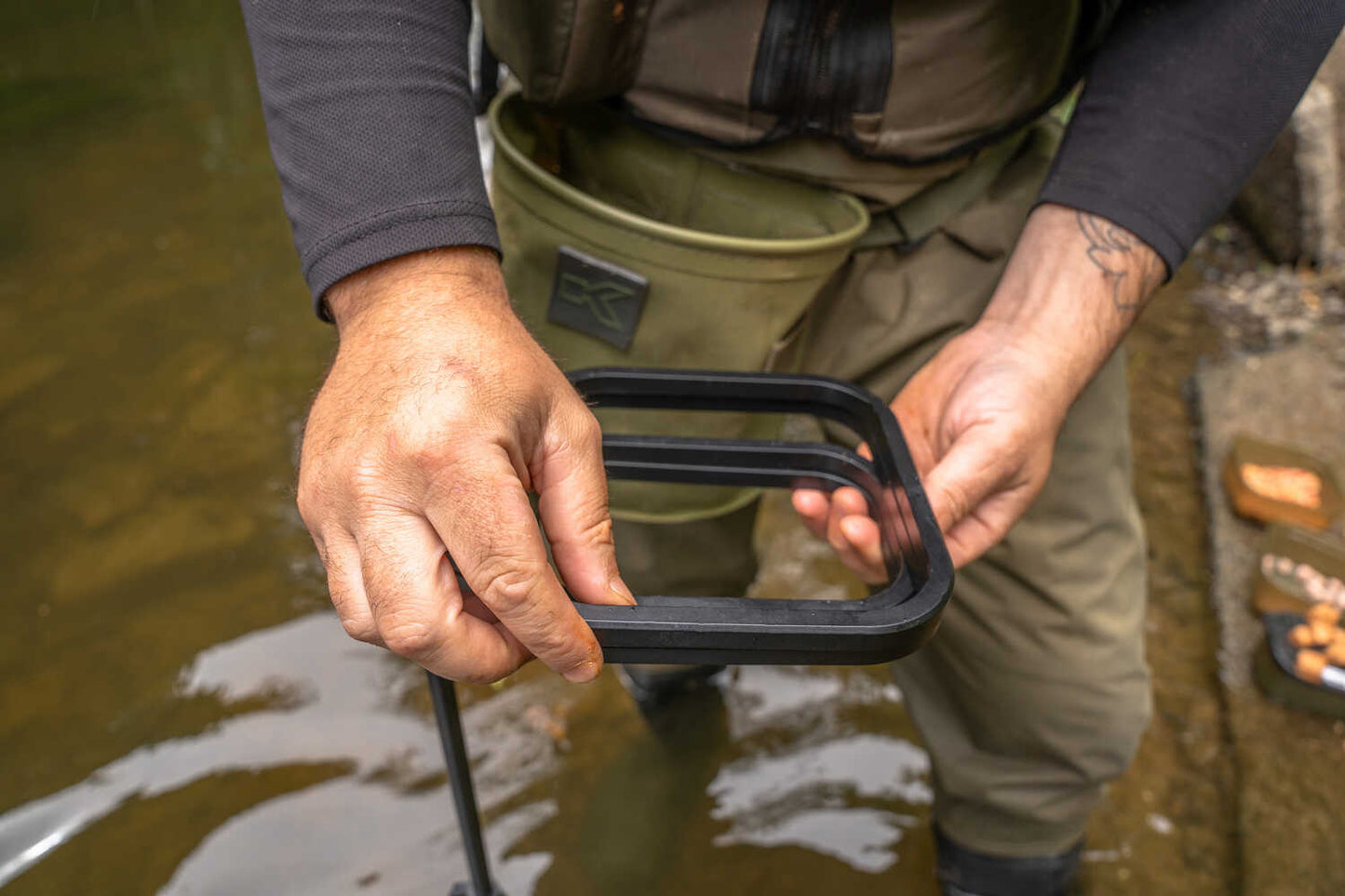 Комплект кутии със стойка KORUM Compact Bait Waiter Set - риболовец, който държи стойка за стръв във вода.