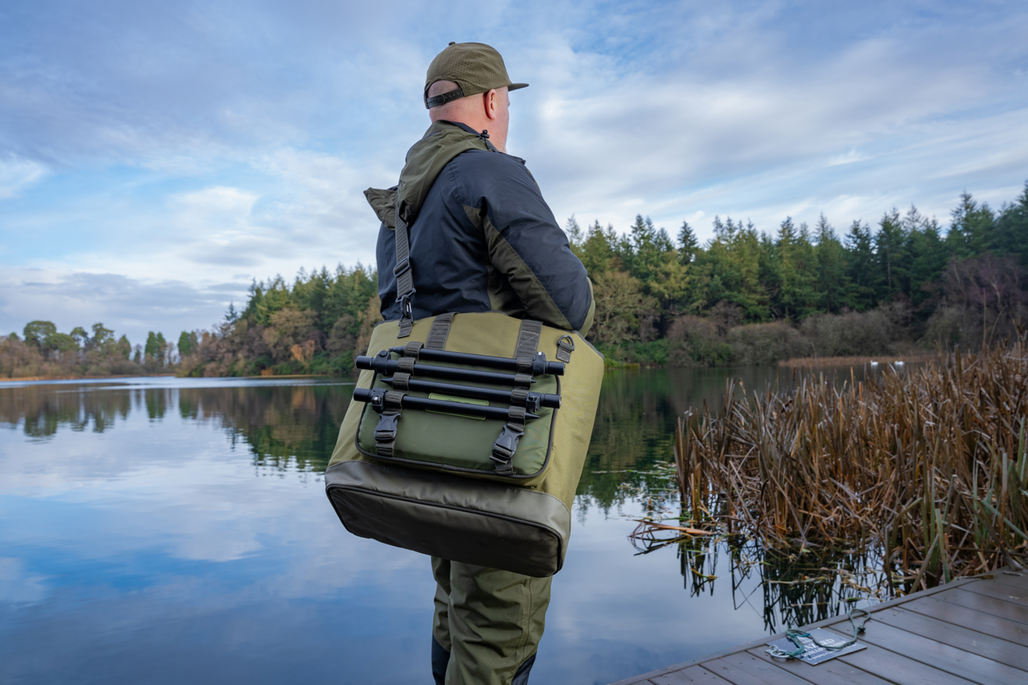 Чанта KORUM Progress Bait & Bits Bag - 25L carried by a person by the water.