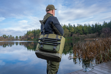 Чанта KORUM Progress Bait & Bits Bag - 25L carried by a person by the water.