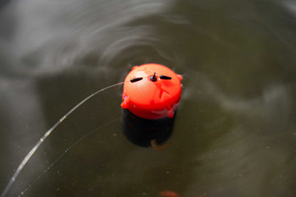 Плуваща фидер хранилка KORUM Floating Feeder, червена с прозрачна рибарска нишка на повърхността на водата.