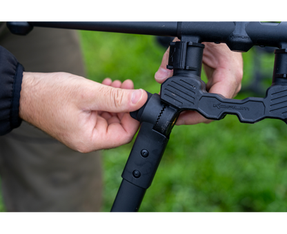 Родпод Korum DELUXE 3 ROD TRIPOD showing user adjusting cam lock mechanism for stability.