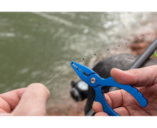 Клещи PRESTON Shot/Stotz Pliers being used to handle fishing line near water.