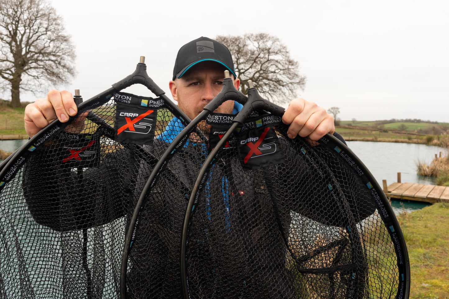 Глава за кеп PRESTON Carp XS Landing Net displayed by an angler at the water's edge, showcasing its design.