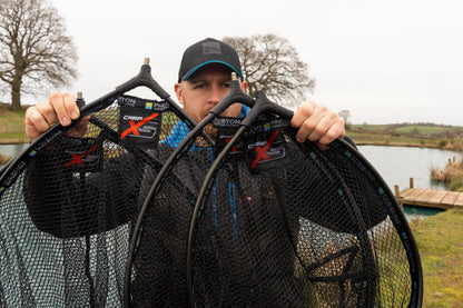 Глава за кеп PRESTON Carp XS Landing Net displayed by an angler at the water's edge, showcasing its design.