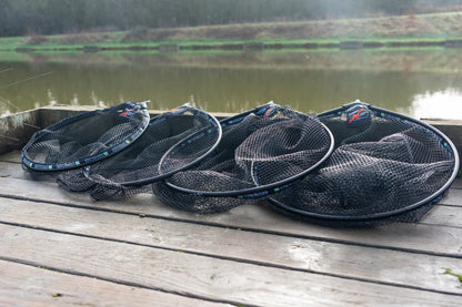 Глава за кеп PRESTON Carp XS Landing Net displayed on a wooden dock by a tranquil water surface.