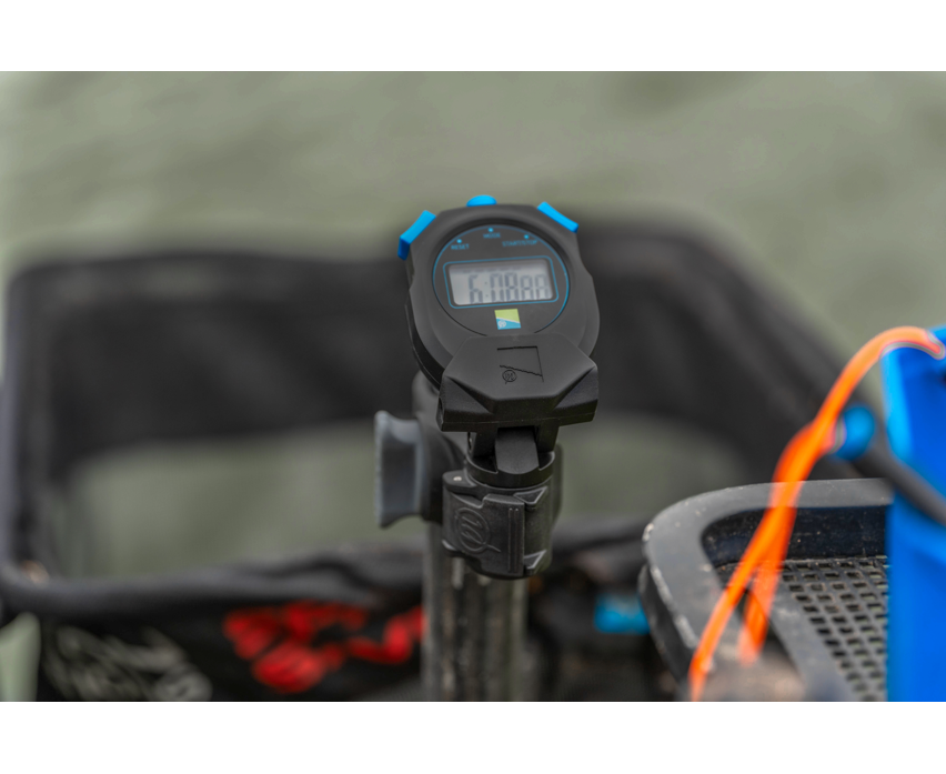 Хронометър PRESTON Offbox Stopwatch displayed on a fishing cart in a natural setting.