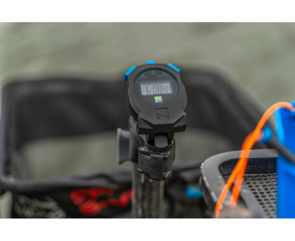 Хронометър PRESTON Offbox Stopwatch displayed on a fishing cart in a natural setting.