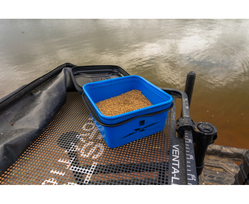 Кутия за стръв PRESTON Supera X Bait Safe Mini with bait on a fishing platform near the water.