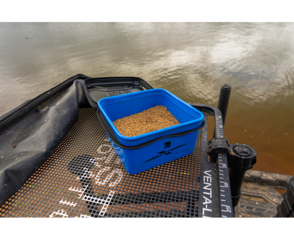 Кутия за стръв PRESTON Supera X Bait Safe Mini with bait on a fishing platform near the water.