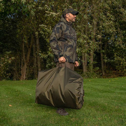 Karп люлка AVID Folda Cradle - Standard/XL carried by a fisherman in camouflage holding carrying bag