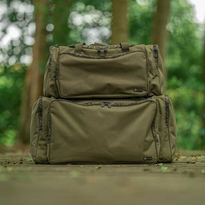 Сак AVID RVS CARRYALL - MEDIUM displayed in a natural outdoor setting with two bags stacked.