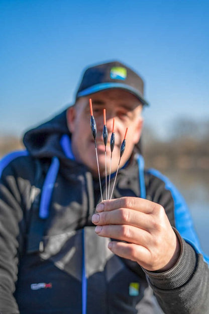 Плувки - PRESTON - CARP XS POLE FLOAT, представени от риболовец, показващ четири плувки на фона на синьо небе.