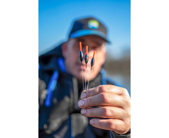 Плувки - PRESTON - EDGE XS POLE FLOAT, представени в ръката на риболовец на фона на синьо небе.