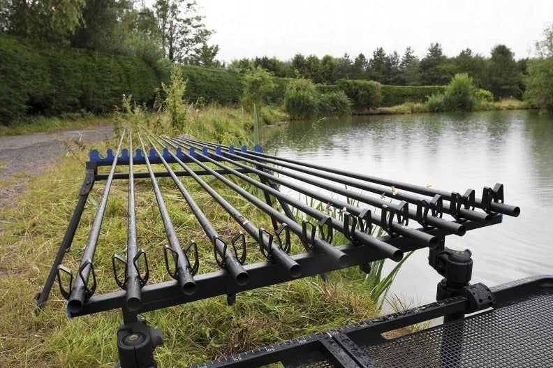 Прикачно PRESTON OFFBOX EXTENDING GRIPPER ROOST with fishing rods near a serene pond.