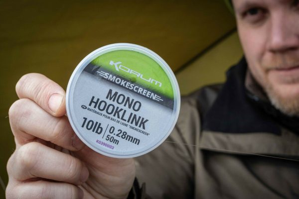 Монофилно влакно за поводи KORUM Smokescreen Mono Hooklink на опаковка, показано от ръка.